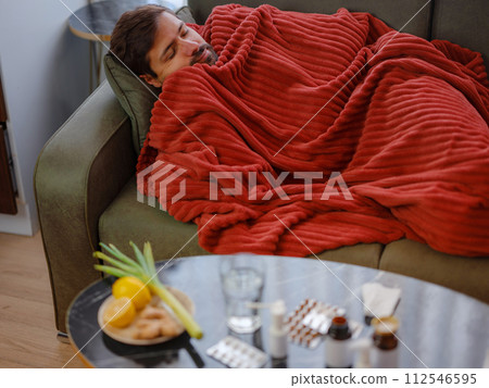 autumn and winter season of sneezes. Young Caucasian Sick man with fever lying on couch . Getting enough restorative sleep helps your body recover and strengthens your immune response. 112546595