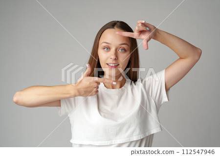Young woman making frame with fingers on a gray background Young woman making frame with fingers on a gray background 112547946