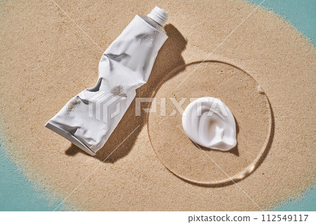 A tube of moisturizing sunscreen and a smear on a sandy background. 112549117