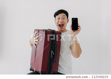 Surprise and wow face of Asian man holding up a suitcase and showing the mobile phone application display. Surprise and wow face of Asian man holding up a suitcase and showing the mobile phone application display. 112549225