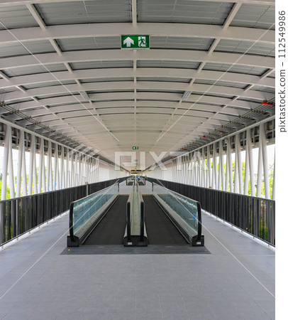 Pedestrian pathway or corridor or hallway with automatic walkway or Moving Sidewalk between train station and building. Pedestrian pathway or corridor or hallway with automatic walkway or Moving Sidewalk between train station and building. 112549986