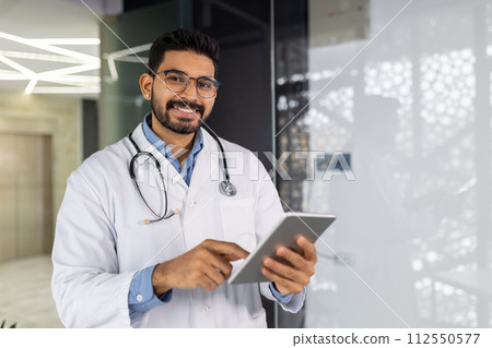 A cheerful male healthcare professional wearing glasses stands in a clinic, holding a digital tablet and radiating confidence. A cheerful male healthcare professional wearing glasses stands in a clinic, holding a digital tablet and radiating confidence. 112550577