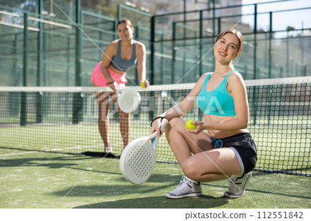 Young women posing with Padel racket in hands next to the net in tennis court 112551842
