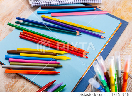 Multicolored pencils and papers on wooden background 112551946