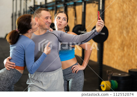 Group of people in activewear take selfies with smartphone after hard workout in cross fitness class with sport equipment 112552074