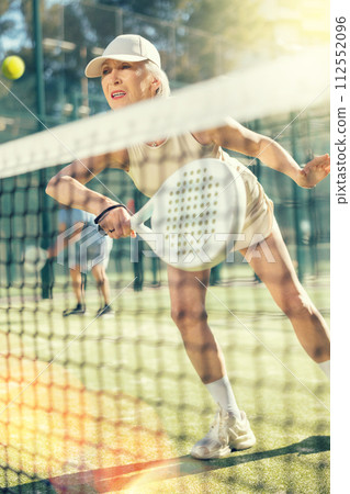 Old woman playing Padel Tennis in open-air tennis court Old woman playing Padel Tennis in open-air tennis court 112552096