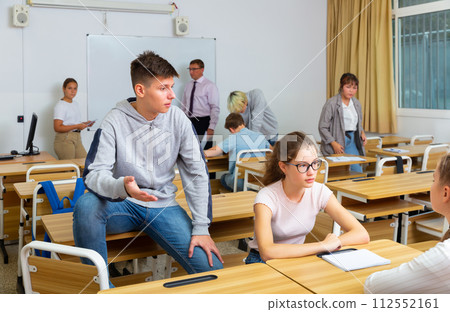 Girl and boy are sitting at the desk and talking about life in classroom. 112552161
