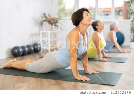 Old woman practicing cobra pose of yoga in training room during fitness classes Old woman practicing cobra pose of yoga in training room during fitness classes 112552179