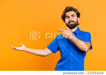 Young man showing thumbs up and pointing at left on blank space, place for your advertisement logo Young man showing thumbs up and pointing at left on blank space, place for your advertisement logo 112552226