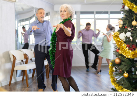 In studio decorated for New Year, elderly man and woman perky dance pair discofox. 112552349