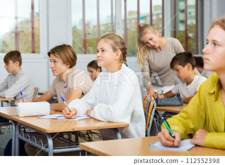 Boys and girls sitting at desk in classroom full of pupils during lesson 112552398