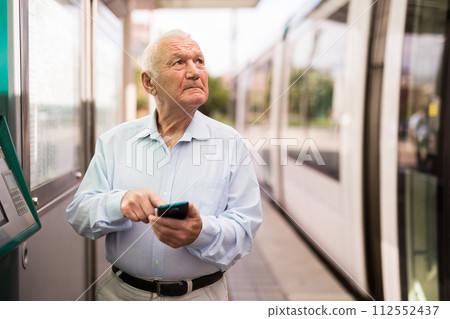 Old man with smartphone on tram stop 112552437