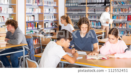 Three schoolchildren writes synopsis in an exercise book from the textbook 112552451