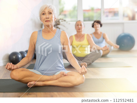 Old woman practicing lotus pose of yoga in training room during fitness classes Old woman practicing lotus pose of yoga in training room during fitness classes 112552481