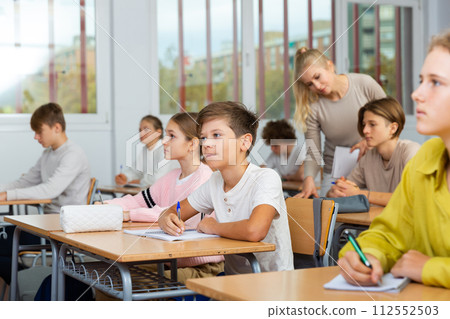 Boys and girls sitting at desk in classroom full of pupils during lesson 112552503