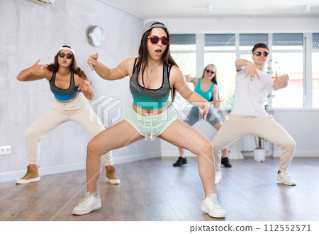 Group of young girls in dark glasses and ball cap and guy dance jazz-funk in fitness club. Group of young girls in dark glasses and ball cap and guy dance jazz-funk in fitness club. 112552571