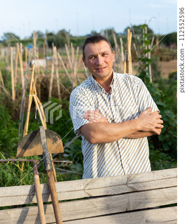 Male farmer posing at fence of his farm on summer day 112552596