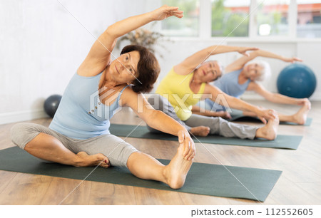 Old woman practicing seated side bend pose of yoga in training room during fitness classes Old woman practicing seated side bend pose of yoga in training room during fitness classes 112552605