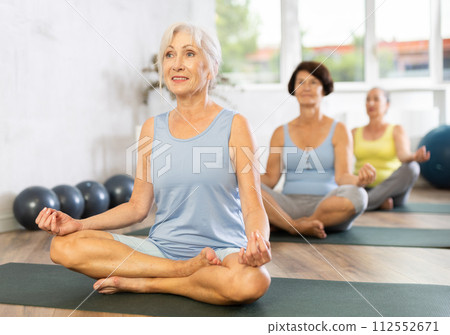 Old woman practicing lotus pose of yoga in training room during fitness classes Old woman practicing lotus pose of yoga in training room during fitness classes 112552671