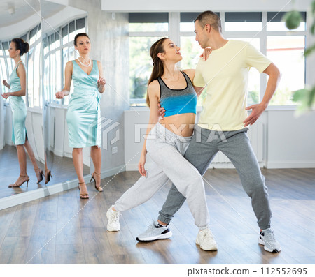 Couple practicing passionate tango guided by female dance instructor in studio 112552695