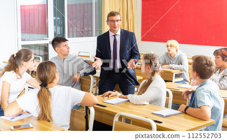 Male teacher giving lesson with interested teenagers in college 112552703