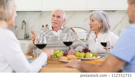 At the table, happy group of adults enjoy their holiday, drink wine and talk together At the table, happy group of adults enjoy their holiday, drink wine and talk together 112552731