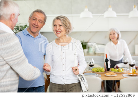 In home, mature man shake hands with couple, say hello, inviting to home family event 112552909