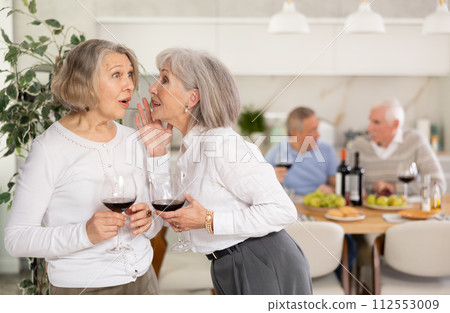 Two elderly women friends hugging in kitchen Two elderly women friends hugging in kitchen 112553009