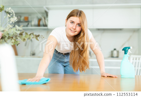 in kitchen,positive housewife in casual clothes holds rag in hands and cleans surface of table in kitchen,positive housewife in casual clothes holds rag in hands and cleans surface of table 112553114