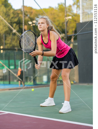 Portrait of concentrated sporty girl with tennis racquet and ball in her hands standing and ready to play match 112553116