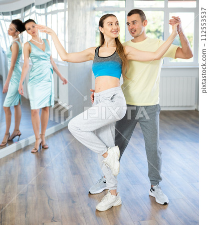 Couple in comfortable sports clothes learns tango dancing during individual lesson Couple in comfortable sports clothes learns tango dancing during individual lesson 112553537