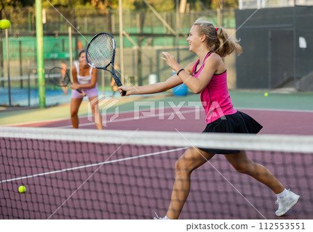 Sporty teenager girl player hitting ball with racket during friendly doubles couple match 112553551