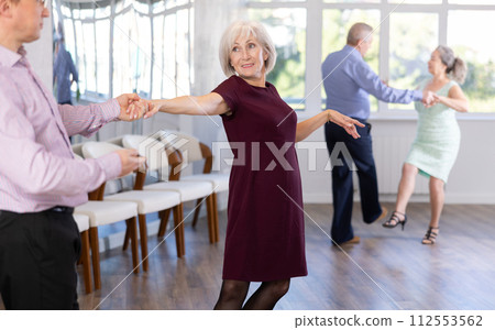 Happy elderly lady with man in elegant clothes dancing bachata in ballroom dance class Happy elderly lady with man in elegant clothes dancing bachata in ballroom dance class 112553562