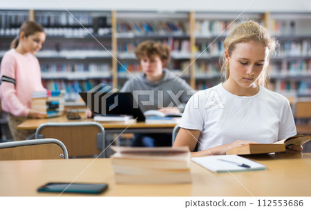 Portrait of teenager girl reading books and writing in notebooks in library 112553686