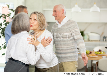 Two elderly women friends hugging in kitchen Two elderly women friends hugging in kitchen 112553862