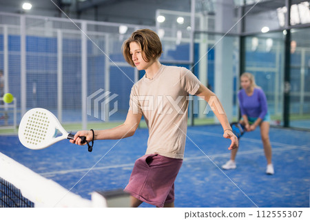 Teenage boy serving ball while playing padel in court 112555307