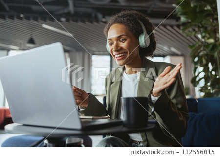 A woman with headphones is seated at a table using a laptop computer 112556015