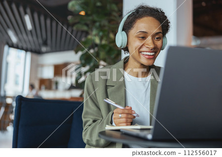 a woman wearing headphones is sitting in front of a laptop computer a woman wearing headphones is sitting in front of a laptop computer 112556017