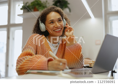 A happy woman sitting at a table with a laptop, wearing headphones and smiling A happy woman sitting at a table with a laptop, wearing headphones and smiling 112556091