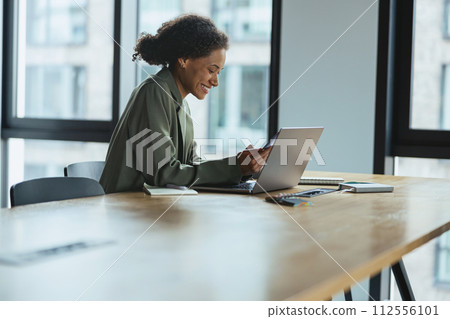 A woman sits at a table using a laptop computer in a building interior 112556101