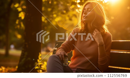 Woman with abdominal pain drinking herbal tea on park bench. 112556769