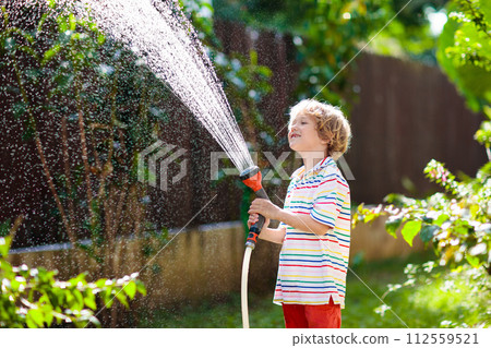 Boy watering flower in garden. Kid with water hose 112559521