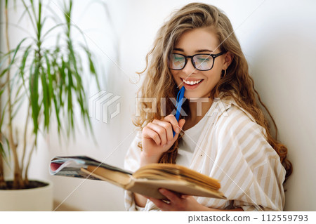 Young woman reading book, writing notes, doing homework at home. Concept of rest, relaxation. 112559793