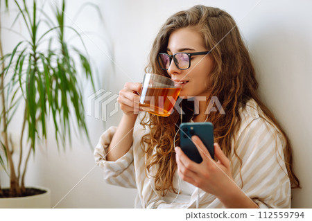Happy woman drinks hot drink and sits on phone, reads book, flips through magazine. Vacation concept Happy woman drinks hot drink and sits on phone, reads book, flips through magazine. Vacation concept 112559794