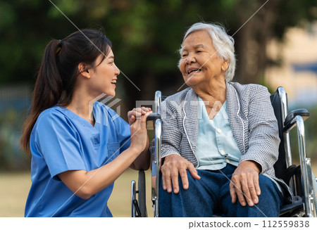 happy nurse take care and talking with senior woman patient in wheelchair at park, friendly caregiver 112559838