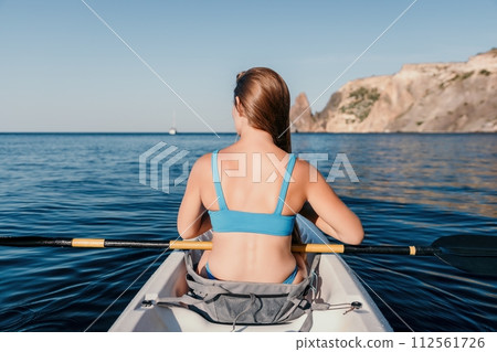 Woman in kayak back view. Happy young woman with long hair floating in kayak on calm sea. Summer holiday vacation and cheerful female people relaxing having fun on the boat. Woman in kayak back view. Happy young woman with long hair floating in kayak on calm sea. Summer holiday vacation and cheerful female people relaxing having fun on the boat. 112561726