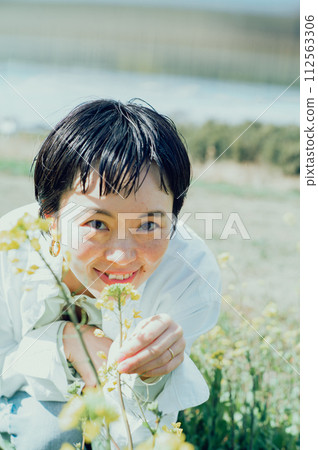 A smiling stylish woman with a short cut admiring flowers outside 112563306