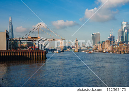 A crisp winter day in London with a clear sky over the River Thames, featuring the Tower Bridge, ongoing riverside construction, and the Shard amidst a dynamic skyline. 112563473