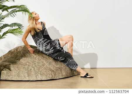 Serene woman in a stylish dress with floral print lounges gracefully on a large rock 112563704