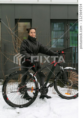 A pretty brunette woman stands with a sports bike in the yard of her house 112564554